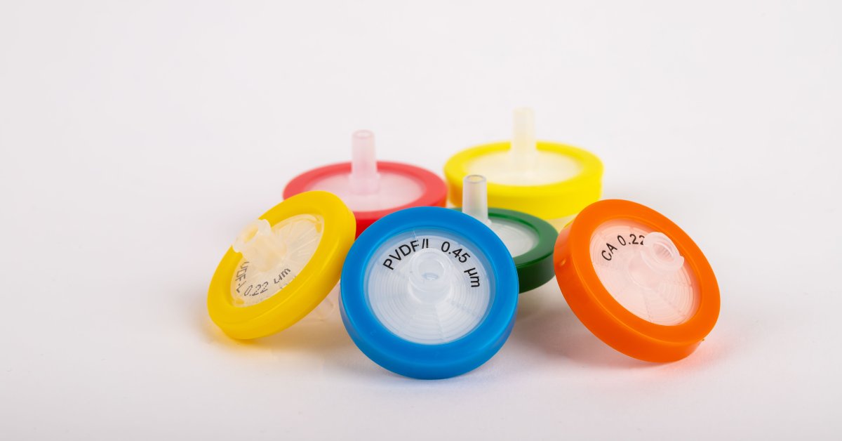 Multiple syringe filters with different color caps and sizes placed next to each other in a circle over a white surface.