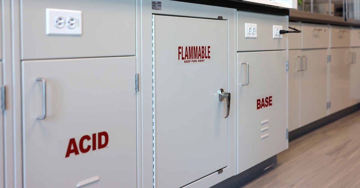 Gray metal chemical storage cabinets labeled with words such as "ACID," "FLAMMABLE," and "BASE" in red letters.