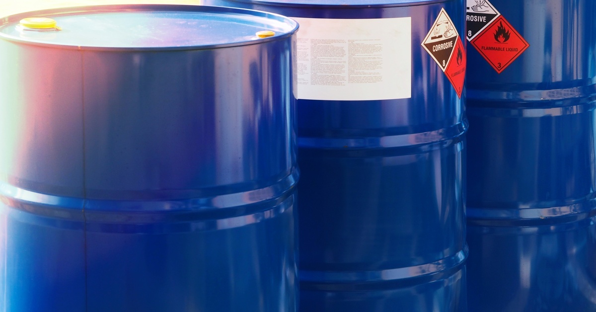 Three blue metal barrels with labels including a black-and-white, diamond-shaped "CORROSIVE" and an orange "FLAMMABLE" symbol.