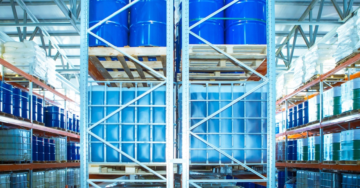 A warehouse area with tall shelves containing plastic and metal chemical containers grouped together.