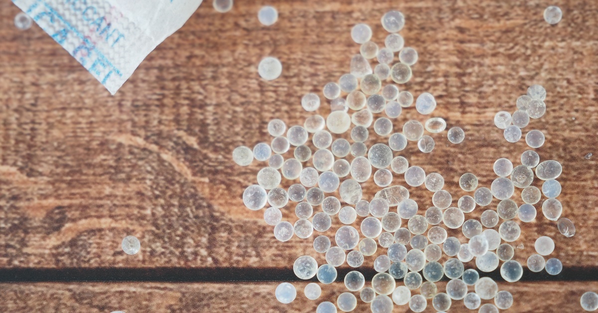 Several silica gel capsules on a wooden surface, with the corner of the packet nearby with warnings not to eat it.